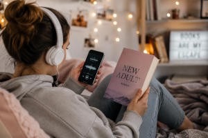 Junge Frau liest New Adult Roman und hoert Hoerbuch ueber Kopfhoerer
